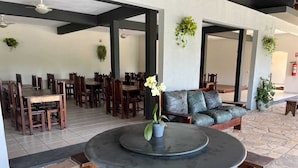 A spacious indoor area with multiple wooden tables and chairs, a central round table, and a green sofa.