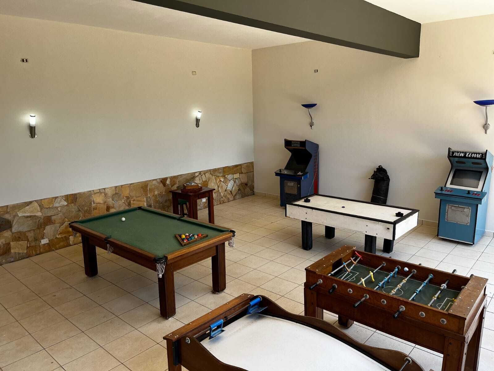 Mesa de billar, mesa de fútbol de mesa y una máquina de videojuegos en una habitación con paredes de piedra y piso de baldosas.
