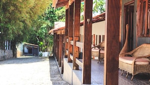 A covered outdoor area with wooden pillars, a stone pathway, and wicker furniture.