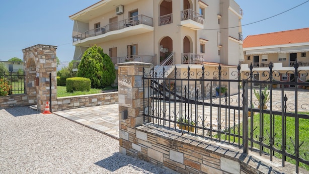 A multi-story building with balconies, a stone entrance, and a gated driveway.