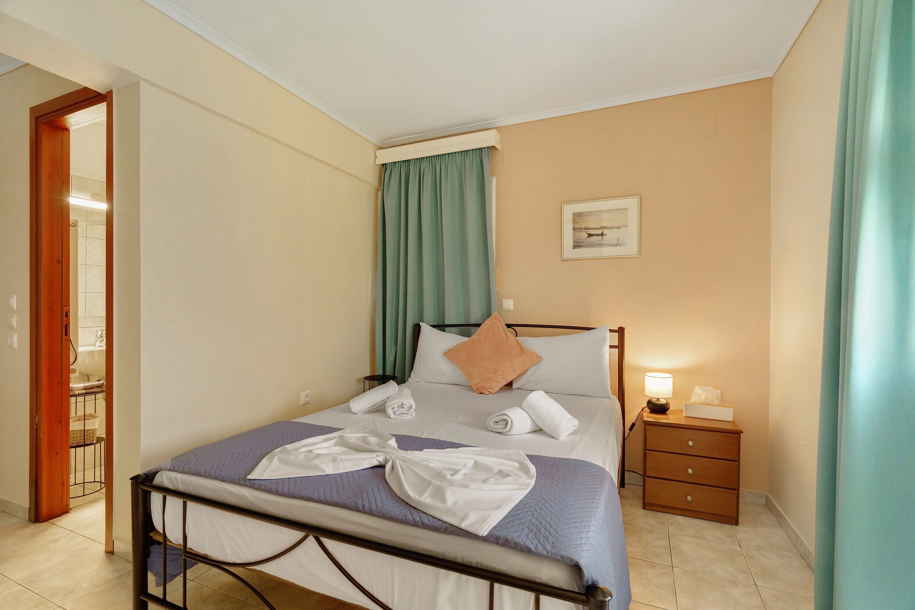 Een hotelkamer met een bed, een nachtkastje met een lamp, een aan de muur bevestigd schilderij en een deur naar een badkamer.