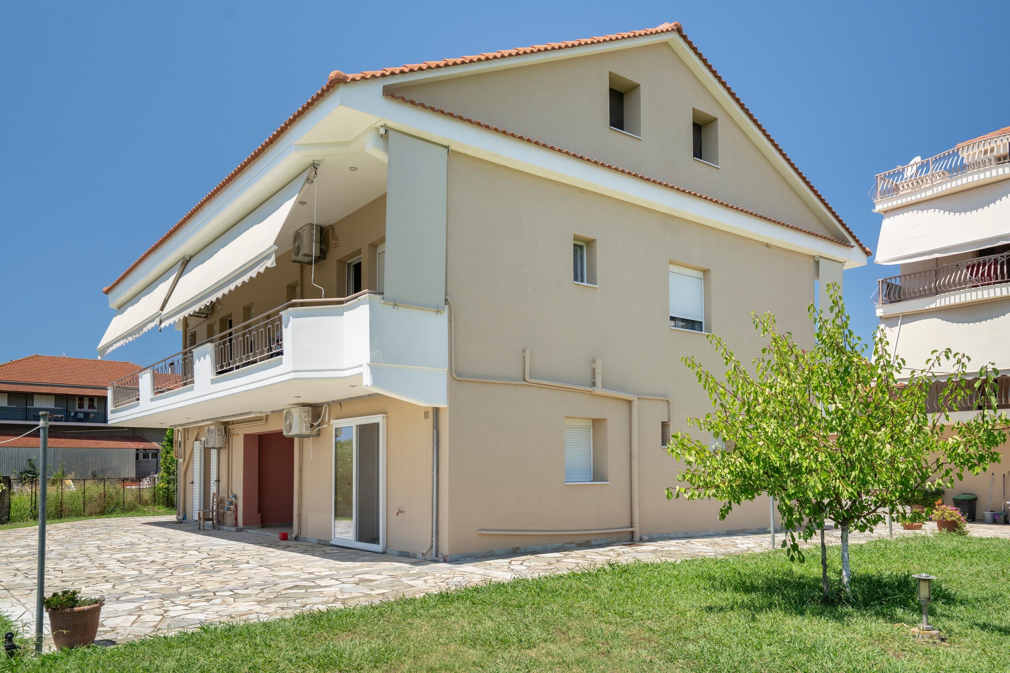 A two-story residential building with a balcony, a tiled patio, and a small tree.