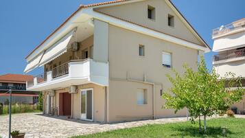A two-story residential building with a balcony, a tiled patio, and a small tree.