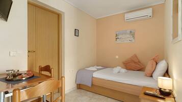 Habitación pequeña con cama, una mesita, una silla, equipo de aire acondicionado y una obra de arte en la pared.