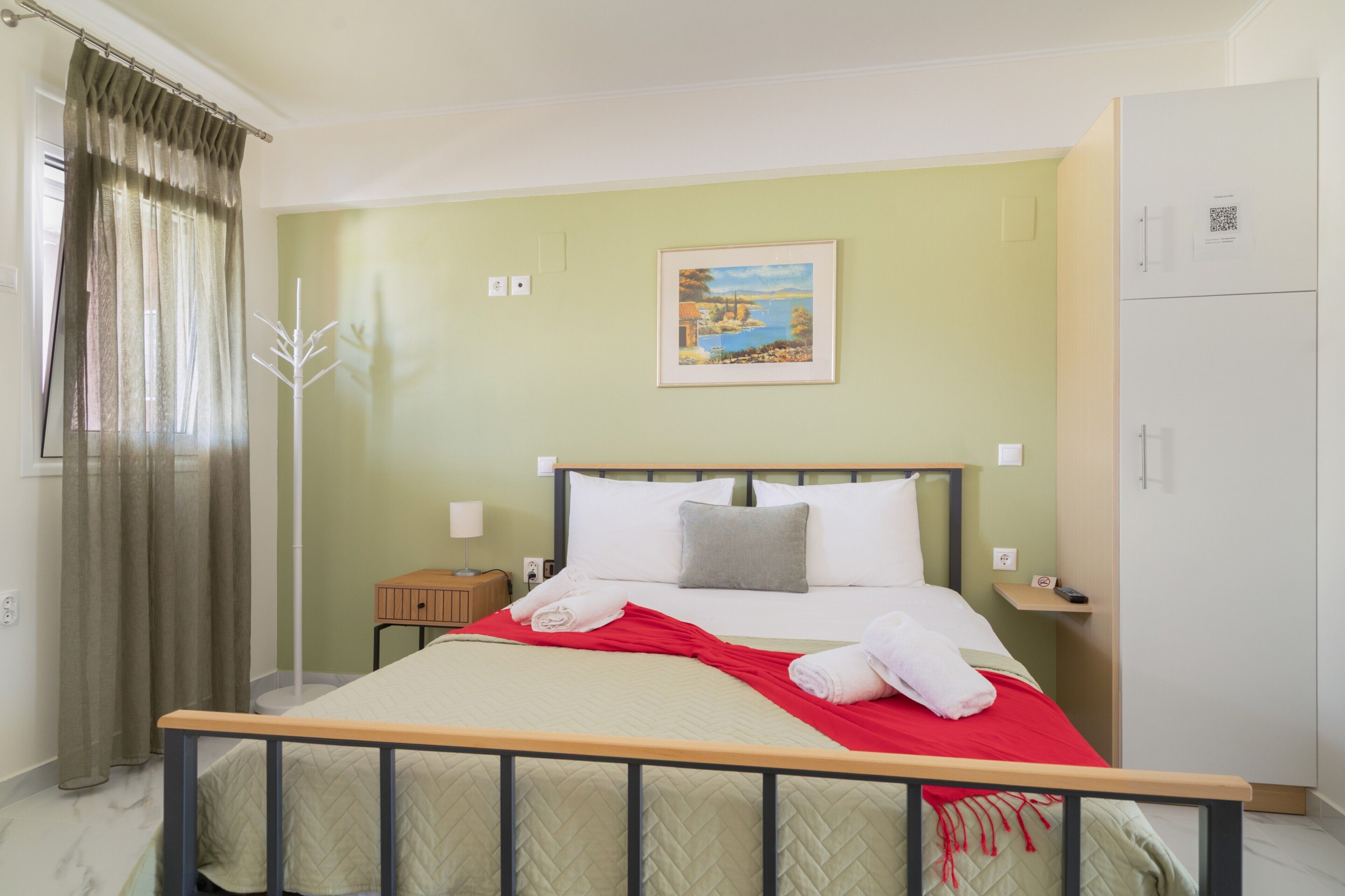 Quarto de hotel com cama, mesa de cabeceira, guarda-roupa, um quadro na parede e janela com cortinas.