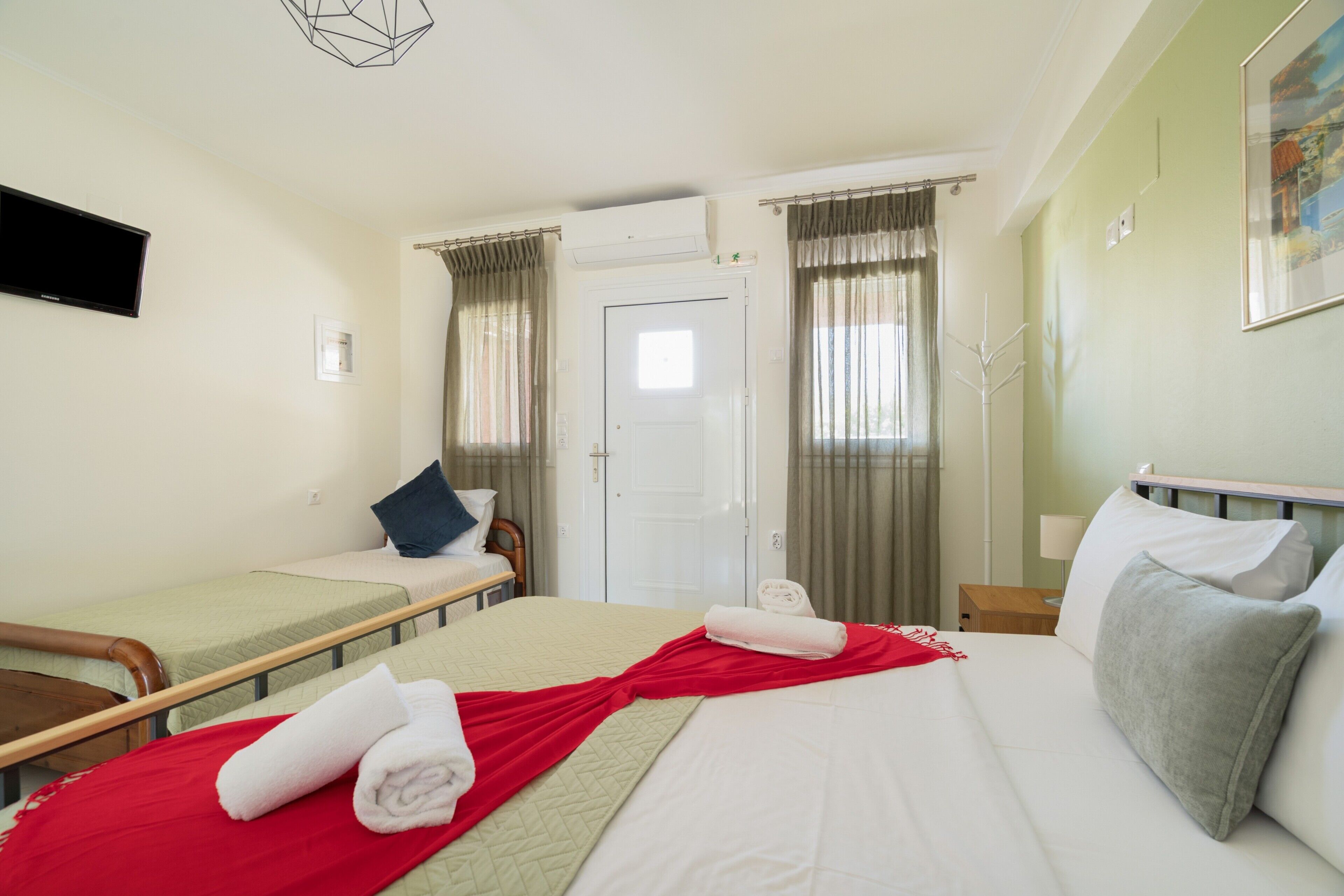 Habitació d'hotel amb dos llits individuals, un llit gran, una televisió de pantalla plana, una porta i una finestra amb cortines.