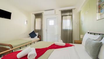 Habitació d'hotel amb dos llits individuals, un llit gran, una televisió de pantalla plana, una porta i una finestra amb cortines.
