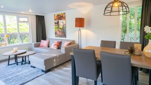 Una sala de estar moderna con un sofá, una mesa de comedor con sillas, una lámpara y un cuadro en la pared.
