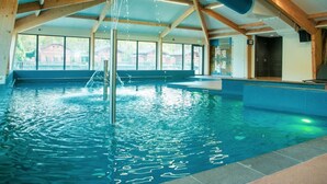 Una piscina interior con una fuente de agua, vigas de madera y ventanas amplias.