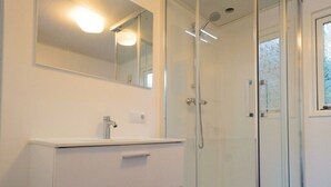 Un baño con ducha de vidrio, tocador blanco con espejo y ventana.