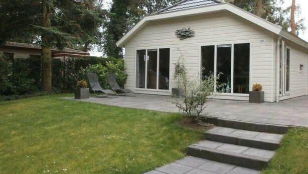 Una casa de un nivel con un porche cubierto, un pequeño jardín con césped y dos sillones de descanso.