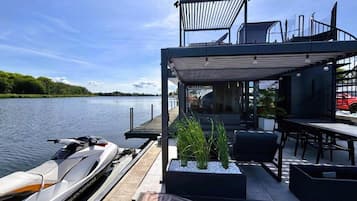 Une terrasse extérieure moderne avec un espace repas, un bateau et une vue sur l’eau.