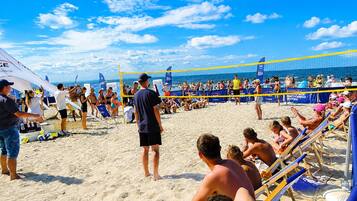 A beach volleyball game with spectators on the sand and a clear sky.