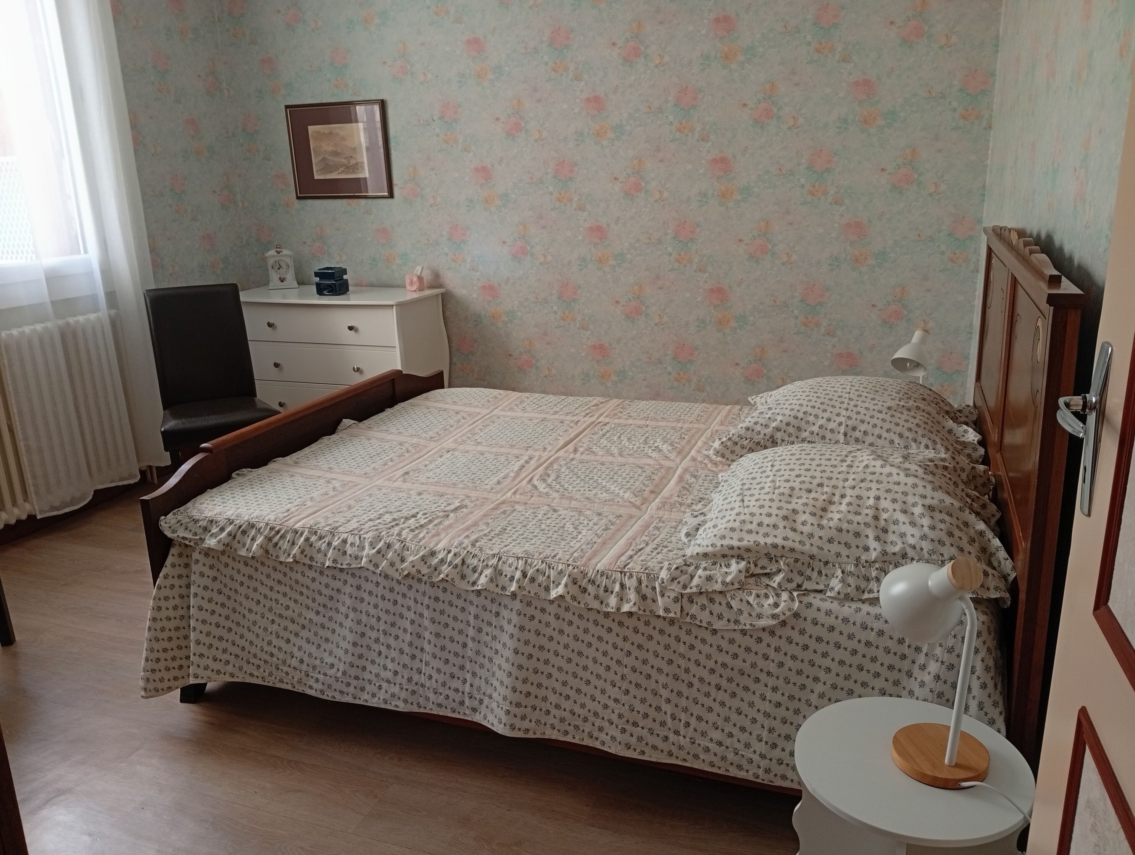 A bedroom with a bed, a bedside table, a lamp, a chair, a dresser, and a framed picture on the wall.