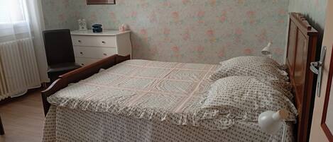 A bedroom with a bed, a bedside table, a lamp, a chair, a dresser, and a framed picture on the wall.