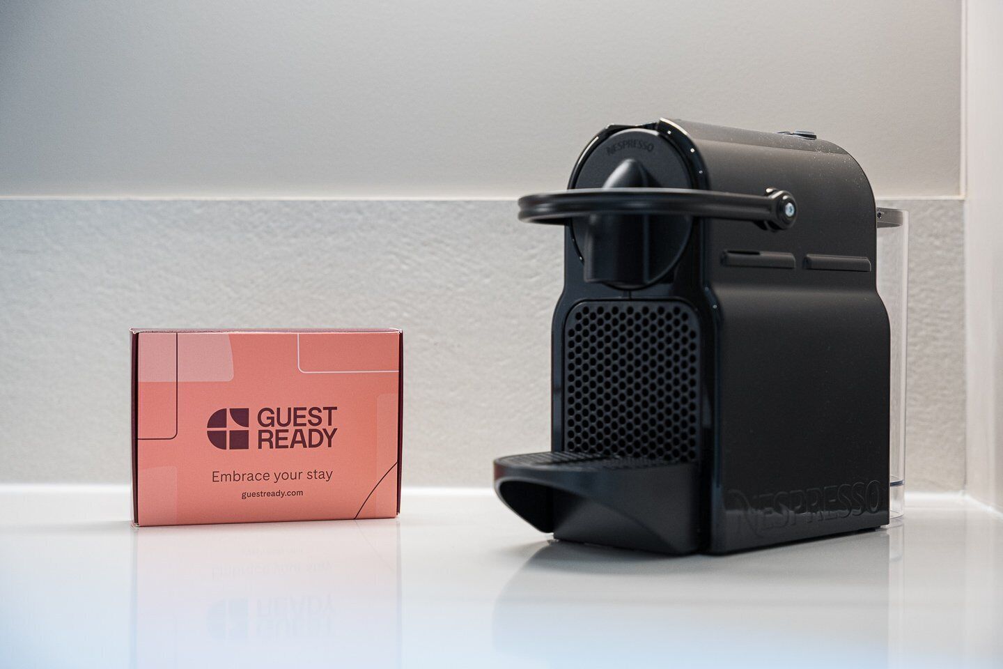 A black coffee machine and a red box labeled 'GUEST READY' with a website address.