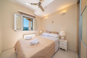 A bedroom with a bed, two bedside tables with lamps, a ceiling fan, a window with blinds, and a star decoration on the wall. - Large villa. Stunning mountain view, 5 mins to beaches at Agia Efimia, Kefalonia (Xiropotamos)