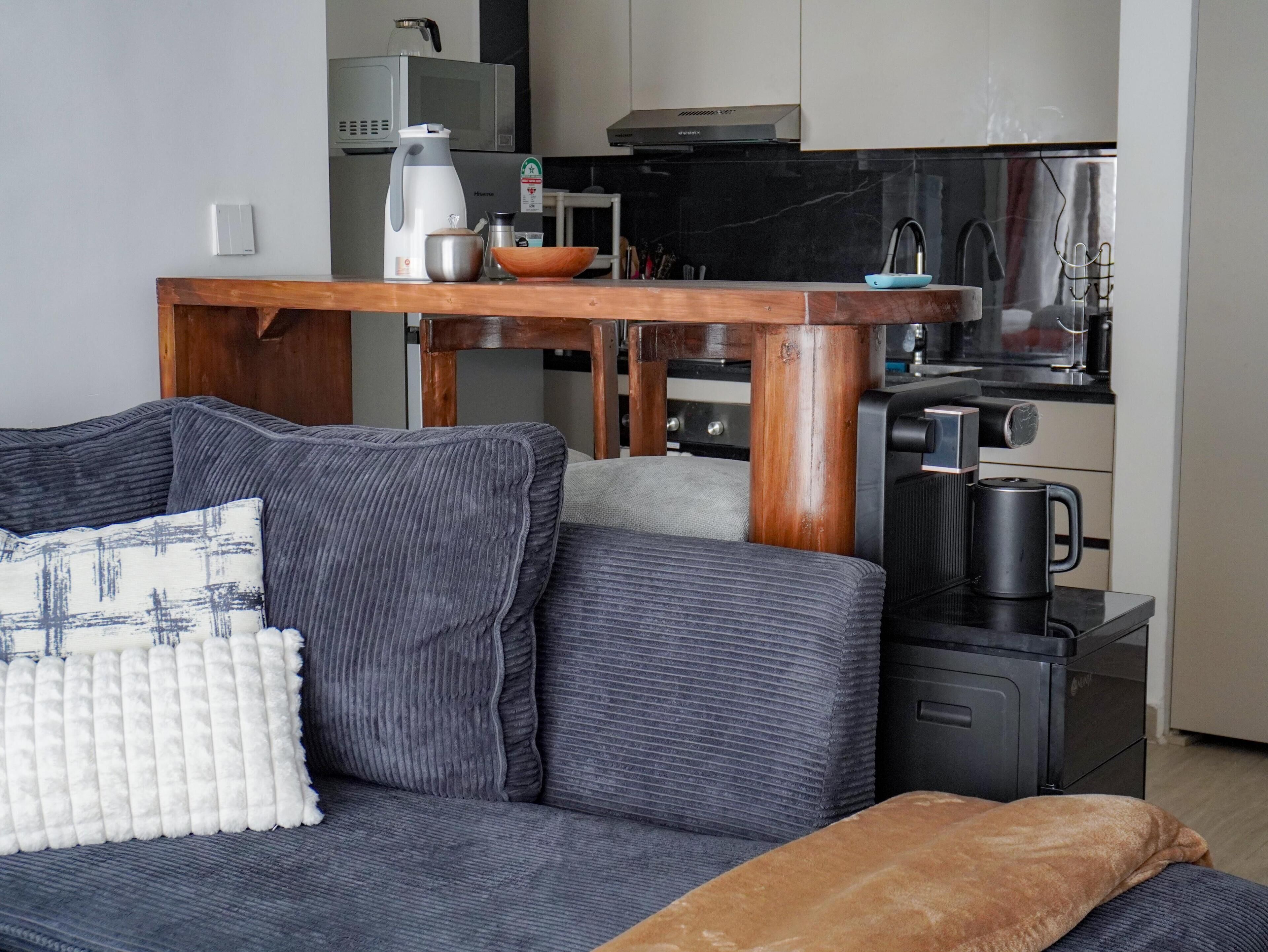 A modern living room with a grey sofa, a wooden coffee table, and a kitchen area in the background.