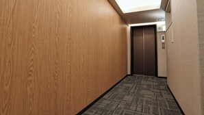 Un couloir aux murs en bois, avec un tapis à motifs et un ascenseur.