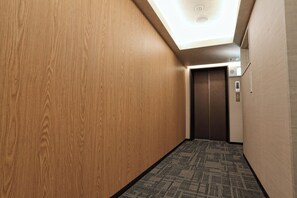 Un couloir aux murs en bois, avec un tapis à motifs et un ascenseur.