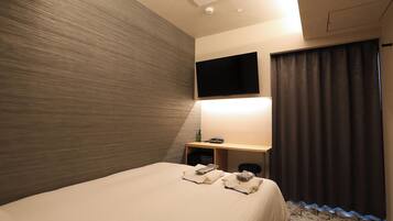 Quarto de hotel com uma cama, televisão de tela plana na parede, escrivaninha com abajur e janela com cortinas.