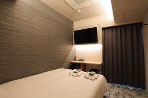 Une chambre d’hôtel équipée d’un lit, d’un téléviseur à écran plat fixé au mur, d’un bureau avec une lampe et d’une fenêtre avec des rideaux.
