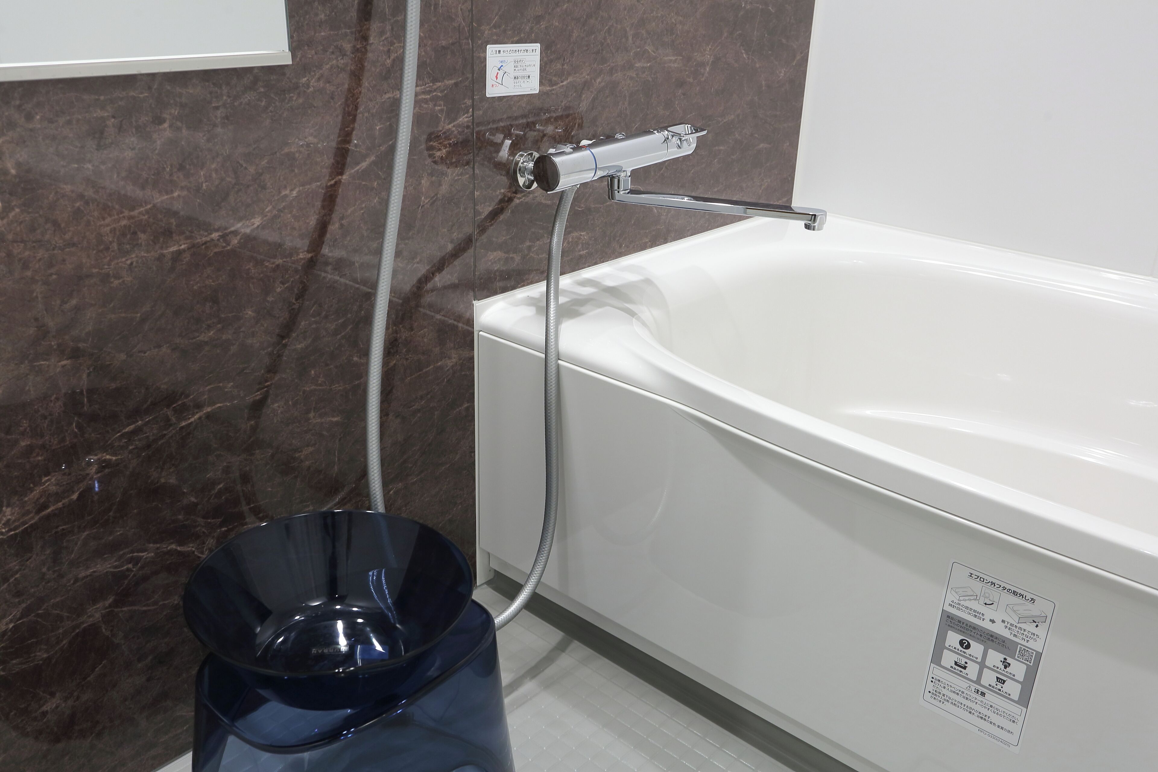 Un baño con una bañera blanca, un cabezal de ducha y un cubo de basura azul.