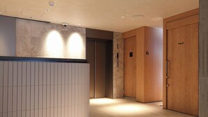 Un hall d’hôtel avec un comptoir d’accueil, une porte en bois portant l’inscription « TOILETTES » et un ascenseur.