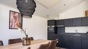 A modern kitchen with dark cabinets, a wooden dining table, and a hanging light fixture. - Holiday Home in Kampen With Terrace (Kampen)
