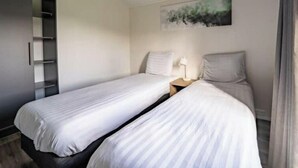 A hotel room with two single beds, a nightstand with a lamp, a wardrobe, and a painting on the wall. - Holiday Home in Kampen With Terrace (Kampen)