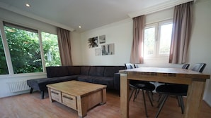 Ein modernes Wohnzimmer mit einer Eckcouch, einem Holztisch und einem Esstisch mit Stühlen.
