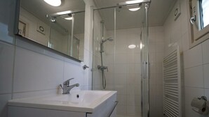 Ein Badezimmer mit einem weißen Waschbecken, einem Spiegel, einer Duschkabine aus Glas und einem Handtuchhalter.
