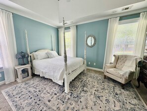 Ein Bett mit Baldachin, ein Nachttisch mit Lampe, ein Sessel und ein Spiegel an der Wand.