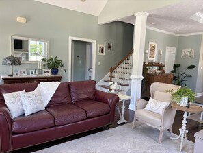 Una sala de estar con un sofá de cuero marrón oscuro, un sillón blanco y una mesita redonda con una planta.