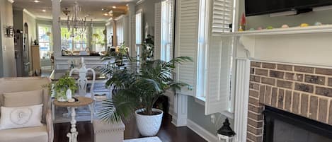 A spacious living room with a fireplace, a chandelier, and a large potted plant.