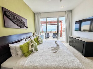 Quarto de hotel com cama, televisão, varanda com vista para a praia e uma grande obra de arte na parede.
