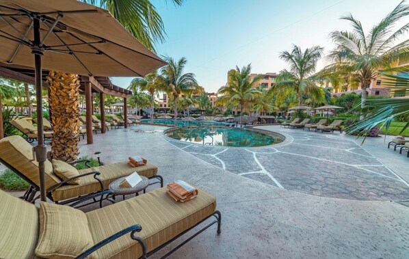 Un espace aménagé au bord de la piscine, avec des chaises longues, des parasols et des palmiers.
