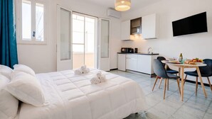 Une chambre d’hôtel comprenant un lit, une table à manger avec des chaises, un coin cuisine et un téléviseur fixé au mur.