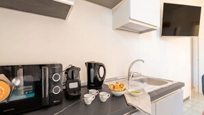 Une cuisine moderne équipée d’un four à micro-ondes encastré, d’une machine à café et d’une bouilloire, d’un évier et d’un téléviseur à écran plat fixé au mur.