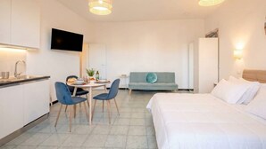 Une chambre d’hôtel moderne comprenant un lit, un canapé, un coin repas avec des chaises, un téléviseur fixé au mur et un coin cuisine avec un évier et des placards.
