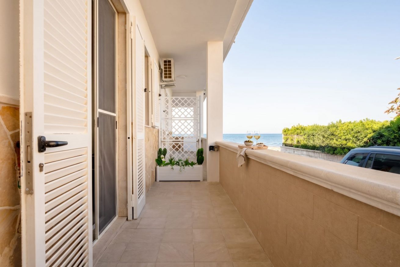 Ein schmaler Balkon mit Blick auf das Meer, eine weiße Tür und ein kleines Pflanzenarrangement.