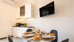 Un coin repas avec une table dressée pour quatre personnes, un téléviseur à écran plat fixé au mur et un coin cuisine équipé d’un four à micro-ondes et d’un grille-pain.