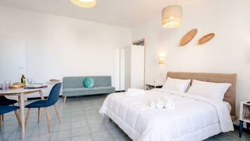 A hotel room with a bed, a dining table with chairs, a sofa, and a small table with a lamp.