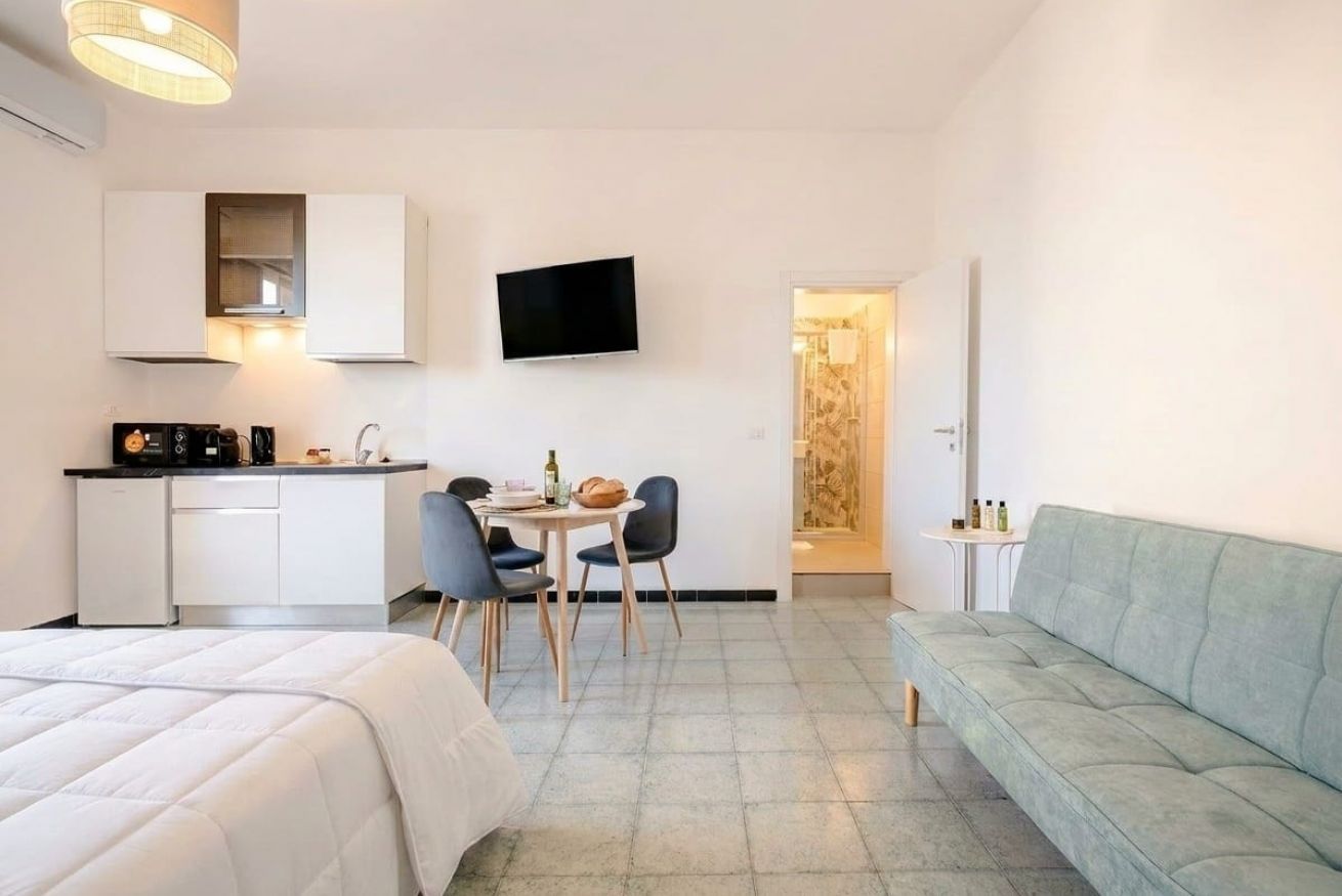 Une chambre d’hôtel compacte comprenant un lit, une kitchenette, un coin repas avec des chaises, un téléviseur à écran plat et un canapé.
