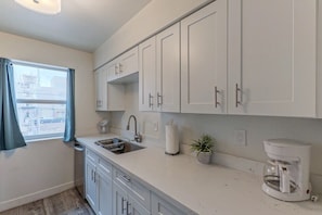 A kitchen with white cabinets, a sink, a coffee maker, and a window with curtains.