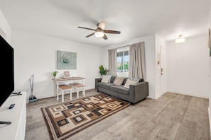 A modern living room with a grey sofa, a coffee table, a ceiling fan, and a patterned rug.