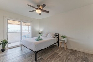 A bedroom with a bed, ceiling fan, bedside table, and a potted plant.