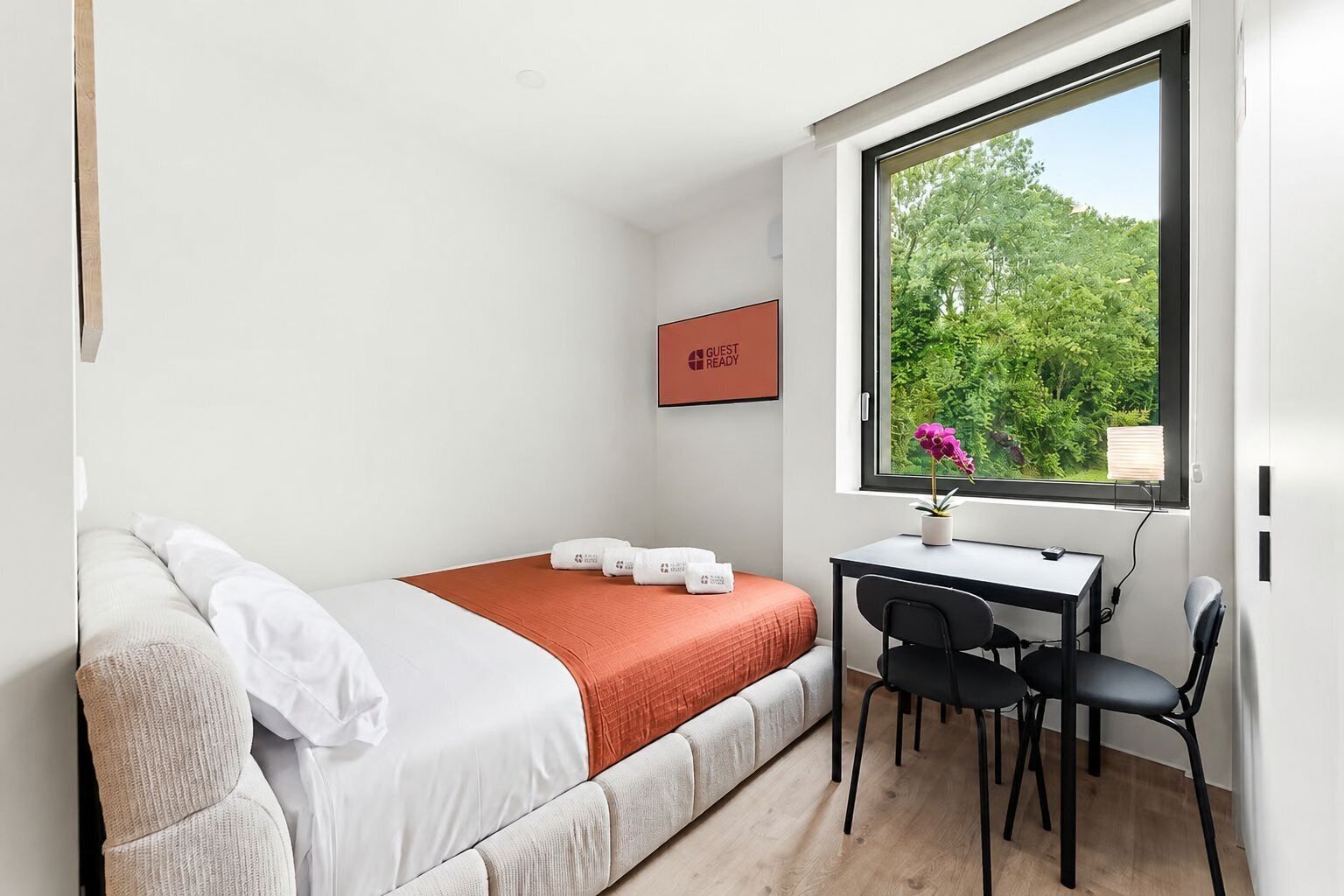 A small, modern room with a bed, a desk, and a window.