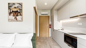 Una camera d'albergo compatta con un letto, angolo cottura e una porta che dà su un'altra stanza.
