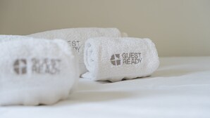 Tres toallas blancas dobladas sobre una cama, con el texto 'GUEST READY'.